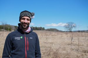 Gus Goodwin wears a TNC jacket and hoodie and smiles at the camera.
