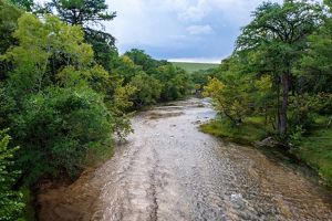 A clear river with a rocky bottom lined with green trees and brush.