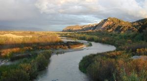 A river winds alongside a plain on one side and a rugged bluff on the other.