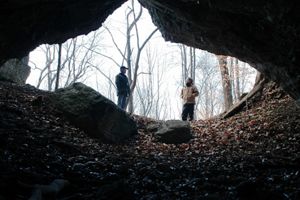 View from inside a cave looking out at two people standing next to the cave's entrance.
