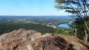 A view from a rock overlook down onto green mountaintops and a river.
