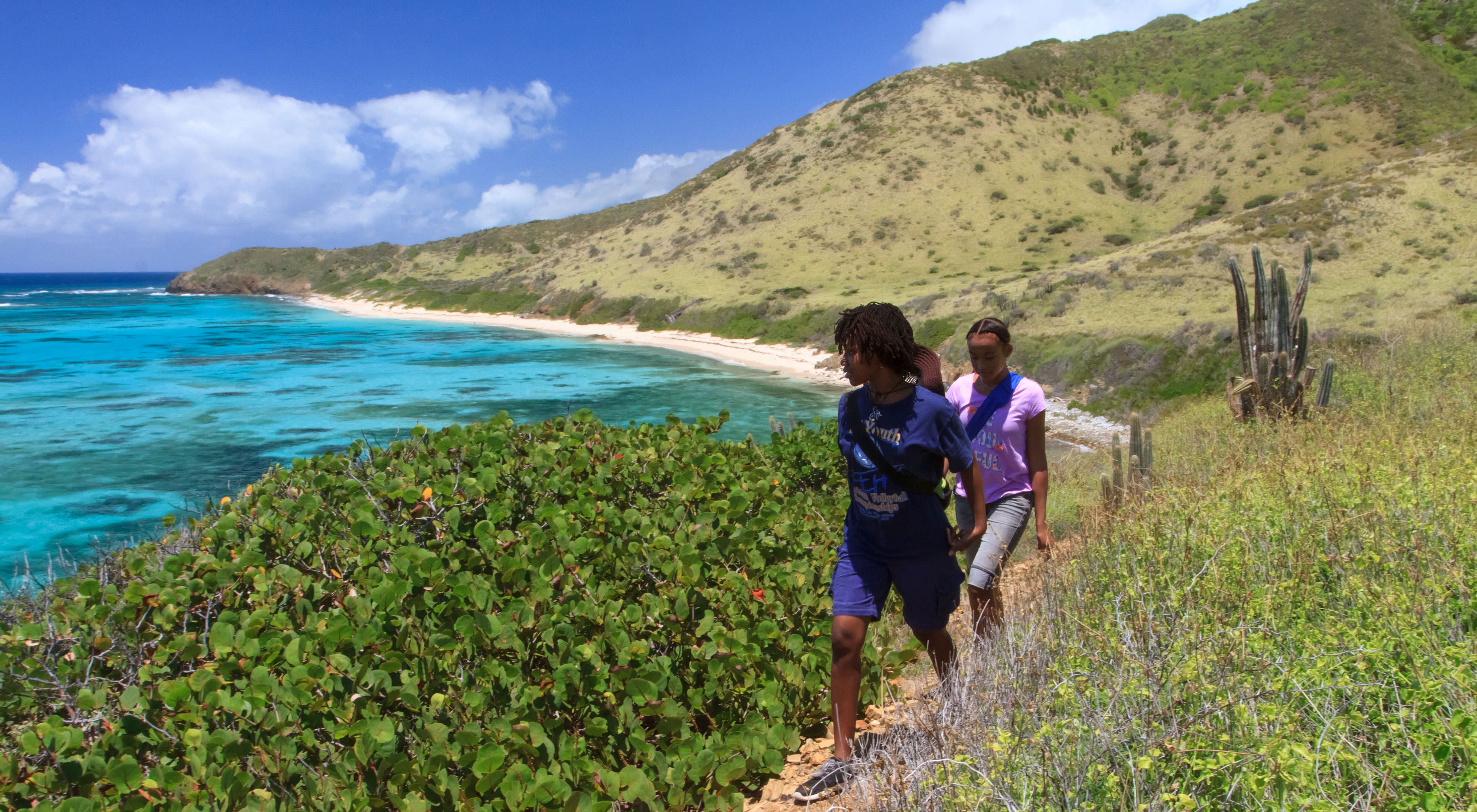 Kids hike along a trail on a hillside overlooking clear, turquoise waters.