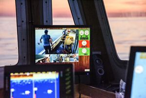 Looking at a monitor inside a fishing boat cabin that shows fishermen at work on the deck.