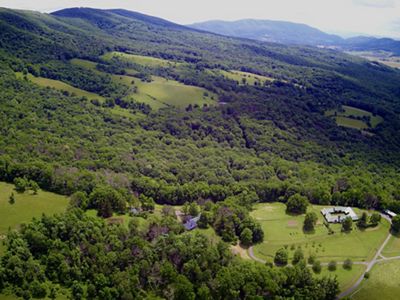 Aerial view looking down on a rural farm. A large farmhouse is nestled in the center of a thick stand of mature trees.