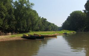 Three canoes and a kayak sit on the side of a river bank.
