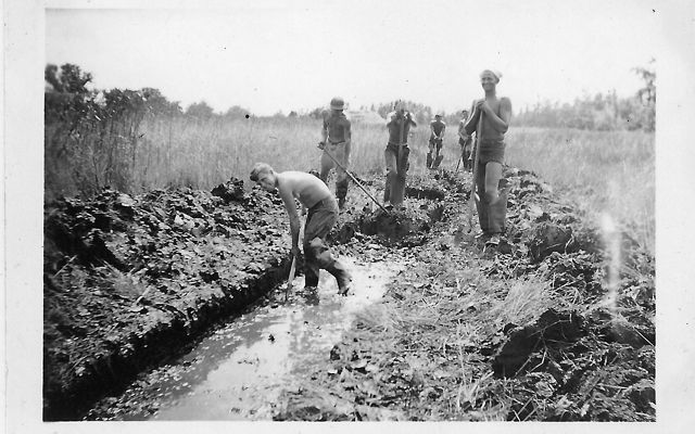 Black and white photo from 1935. Five men holding shovels stand at the end of a wide ditch filled ankle deep with water. One man is in the ditch bent over digging.