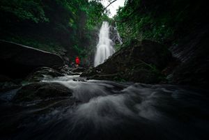 A person stands in front of a magnificent waterfall.