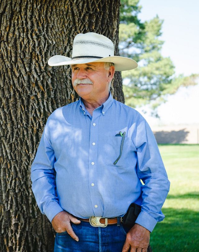A man wearing a white cowboy hat leaning against a tree.