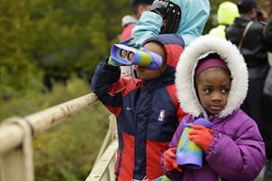 2 young kids at a park in Chicago peer through binoculars specifically made for children.