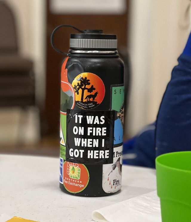 A water bottle with several stickers including one that reads It Was On Fire When I Got Here.