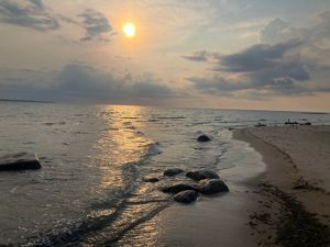 Sun in a hazy sky over waves lapping up against the shore of a lake.