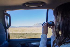 A woman looking through binoculars out of a car window.