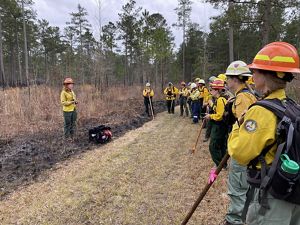 TNC's Laurel Schablein stands at the edge of a grassy field leading a briefing for the group of women assembled around her during a fire learning exchange training.