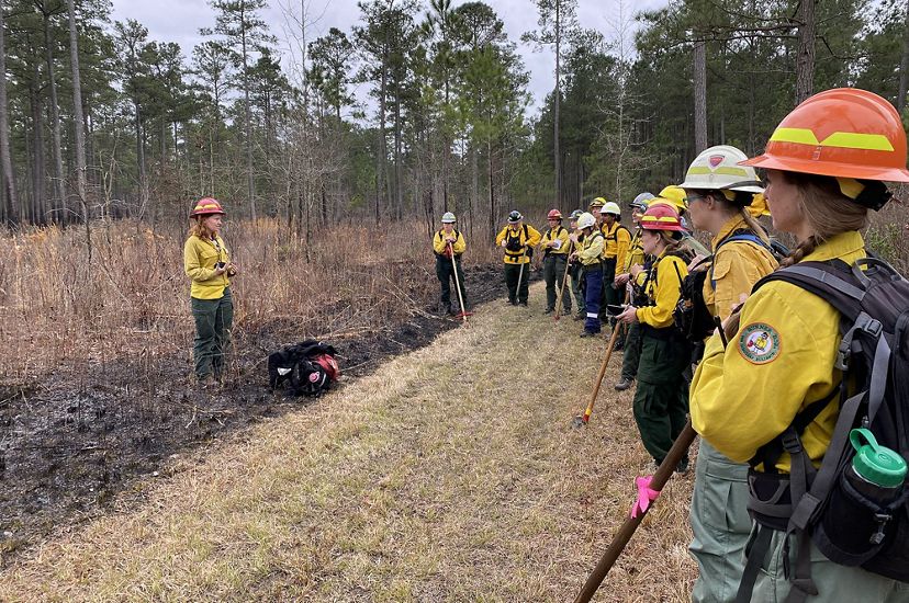 TNC's Laurel Schablein stands at the edge of a grassy field leading a briefing for the group of women assembled around her during a fire learning exchange training.