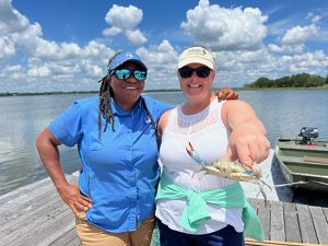 Two people pose with a blue crab on a fishing pier.