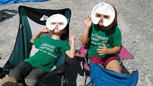Two children wear homemade solar eclipse glasses made from paper plates.