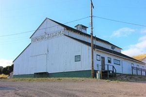 Broad side of a white barn alongside a gravel road under blue sky.