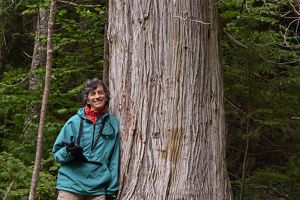 A woman leans against a very large tree.