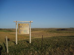 Large sign that reads Jacobson Fen Preserve with rolling prairie landscape in the background.