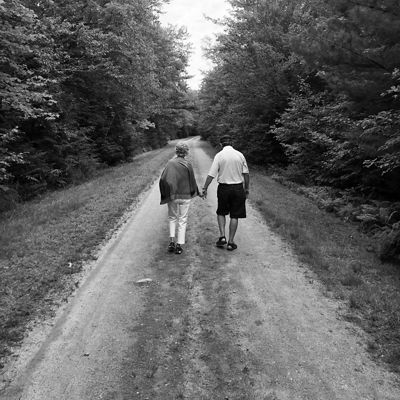 Black and white photo of two people walking down a dirt trail heading away from the camera.