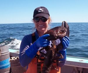 Dr. Jocelyn Runnebaum wears blue rubber gloves and holds up a large lobster while standing on a boat in the ocean.