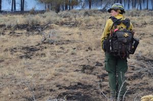 TNC Oregon Burn Boss Katie Sauerbrey stands in fire practitioner gear with their back turned and a forest in front of her.