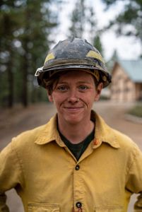 A woman firefighter wearing all of her gear, smiling for a headshot.