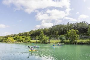 Four kayakers paddle on a blue river.