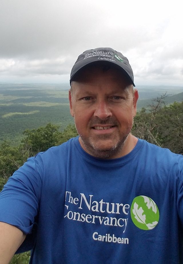 Candid photo of deputy state director Keith Tassin on an overlook of various greenery and clouds in the background.. 