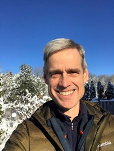 a man with gray hair smiling in front of a snowy mountain