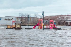 A playground flooded with one to two feet of water at Tennean Beach in Dorchester, with warehouses in the background.