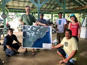 A group of six people pose in an outdoor pavilion holding a large map between them.