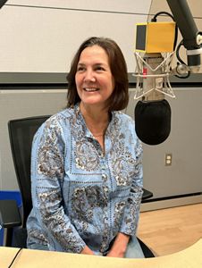 State Director Kris Sarri sits in a chair in front of a microphone recording in the WBUR studio.