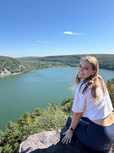 A large body of water serves as the backdrop for a smiling woman sitting on a rock outcrop.
