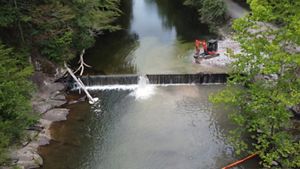 A backhoe works next to a small dam on a river.
