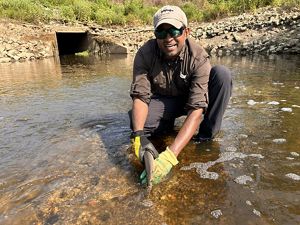 A man holding a fish kneels in shallow water.