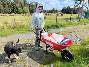 A person with boots and a hoodie pushing a wheelbarrow filled with supplies.