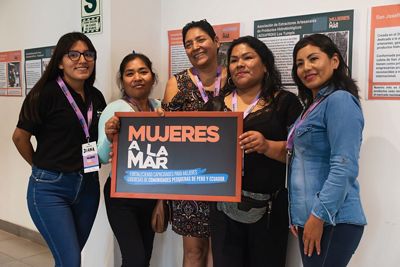5 mujeres sostienen un cartel “Mujeres a la mar” fortaleciendo capacidades de lideresas pesqueras en Ecuador y Peru