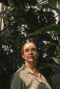 Fotografía de mujer, mirando hacia un punto fijamente, con vegetación en el fondo.