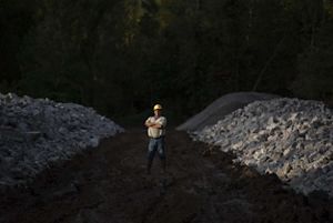 Person standing in yellow hard hat between piles of limestone rocks. 