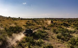 two large trucks driving through an African savannah.