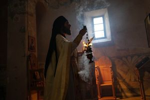 A monk holds a burning censer with a small window in the background.