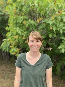 Headshot of Maggie Eshleman in a dark green shirt in front of green leaves.