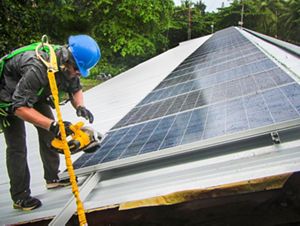 A worker harnessed on a roof installing a solar panel.