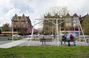 A group of people sit on a swing set in a small area of grass on a city block.
