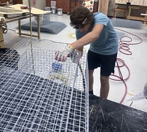 A young adult uses tools to work with wire.