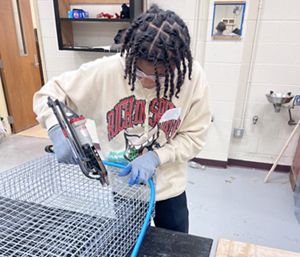 A young adult uses tools to work with wire.