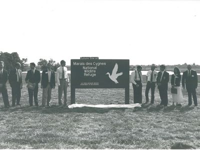 Nine men and 1 woman stands next to entrance sign.