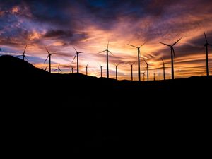 Wind turbines silhouetted against a colorful sky.
