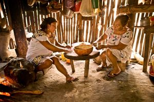 Two people prepare food on a simple table in a family cooking hut in the Maya Forest in Mexico.